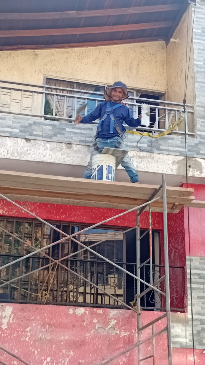 Obrero terminando acabado de fachada desde andamio